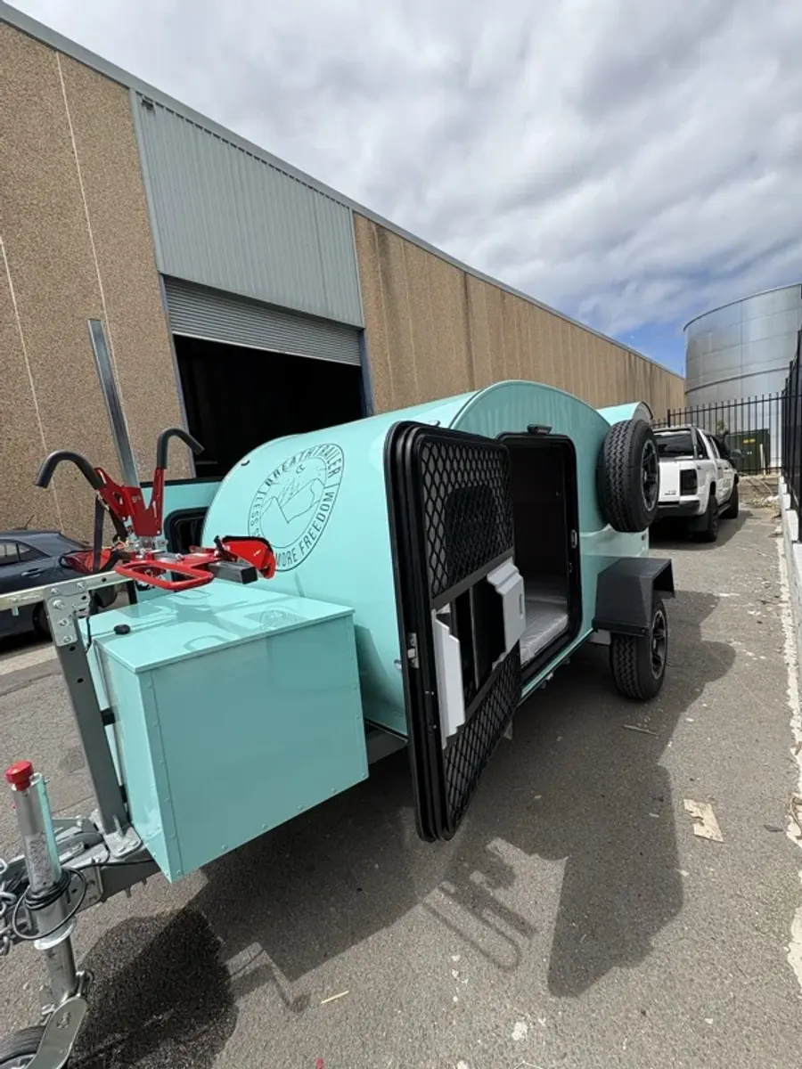 Mint compact Breath teardrop with side door open and bike rack beside a large shed