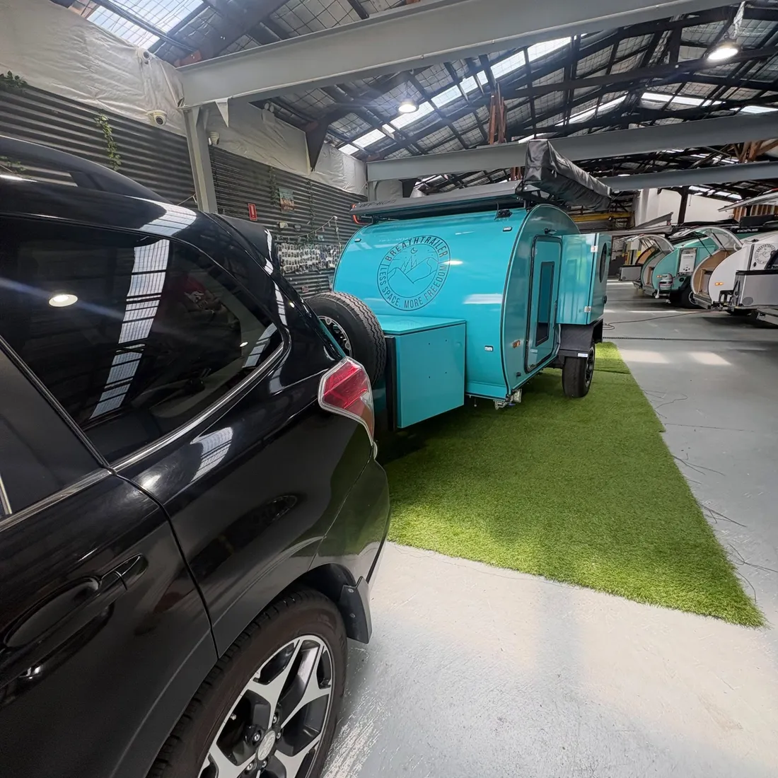 A recent turquoise Breath camper beside its tow vehicle at collection