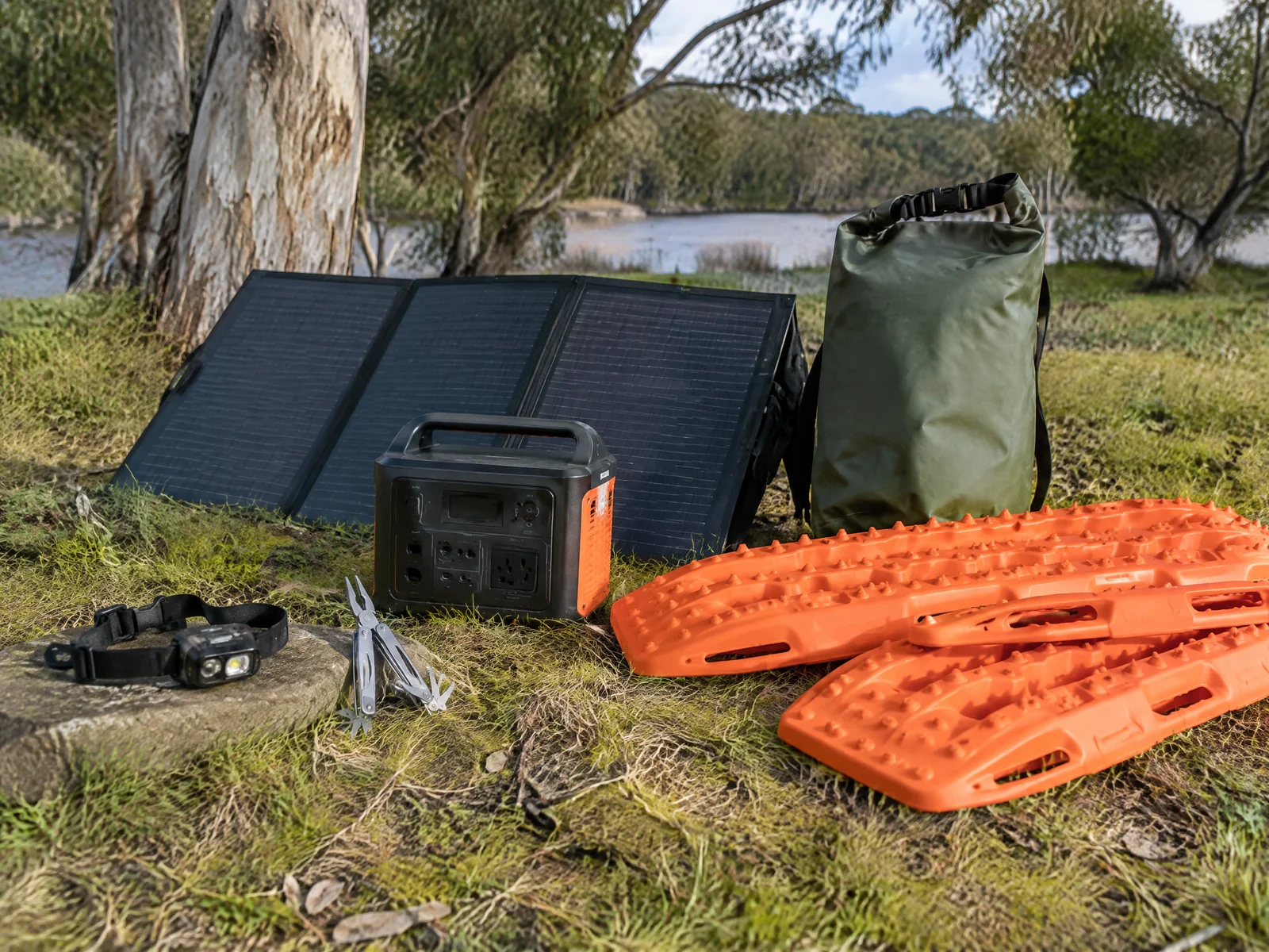 Camping accessories laid out on grass including a headlamp, recovery boards, portable power station and folding solar panel