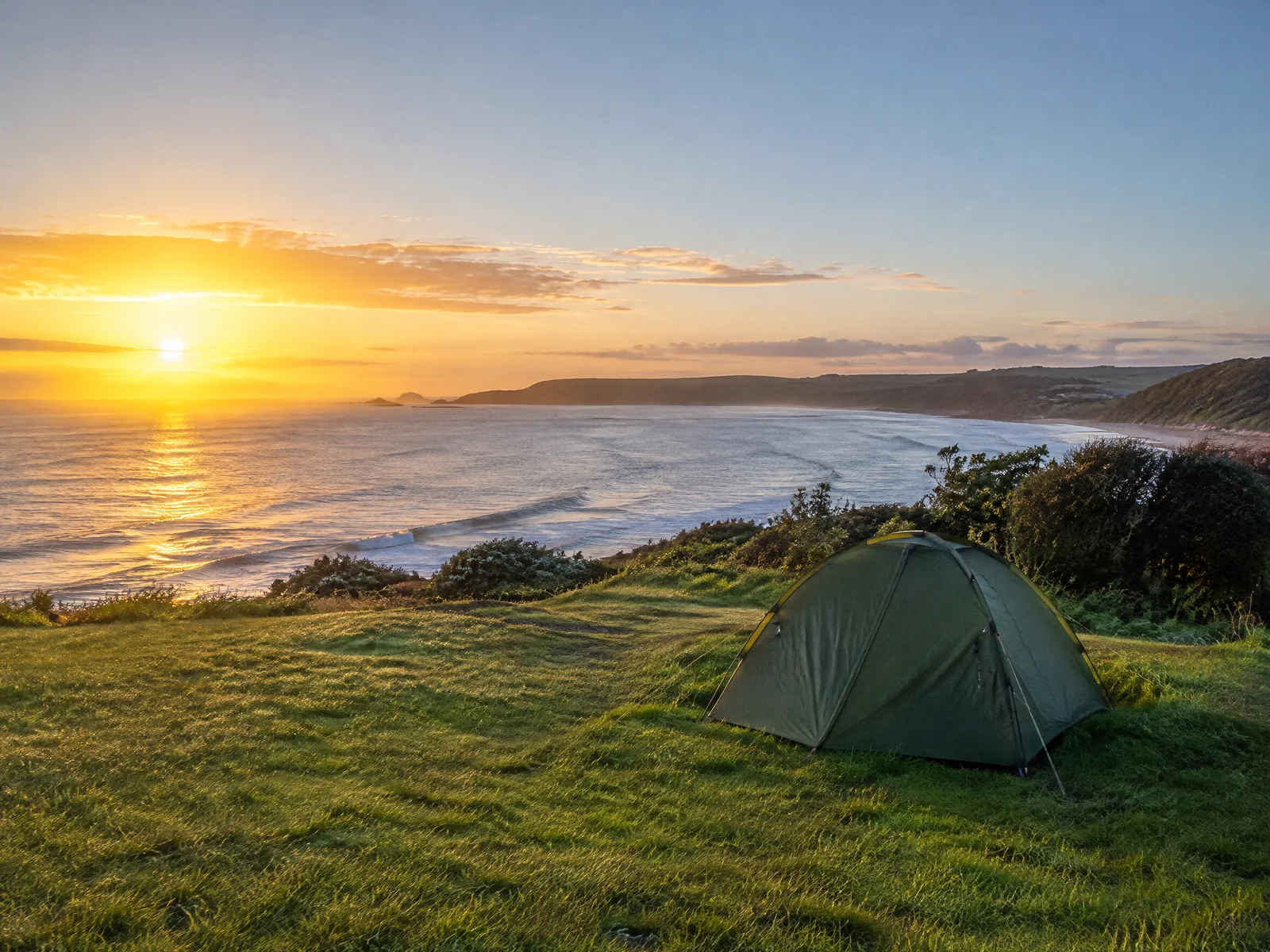 Australian coastal campsite at sunrise with golden morning light over a blue ocean