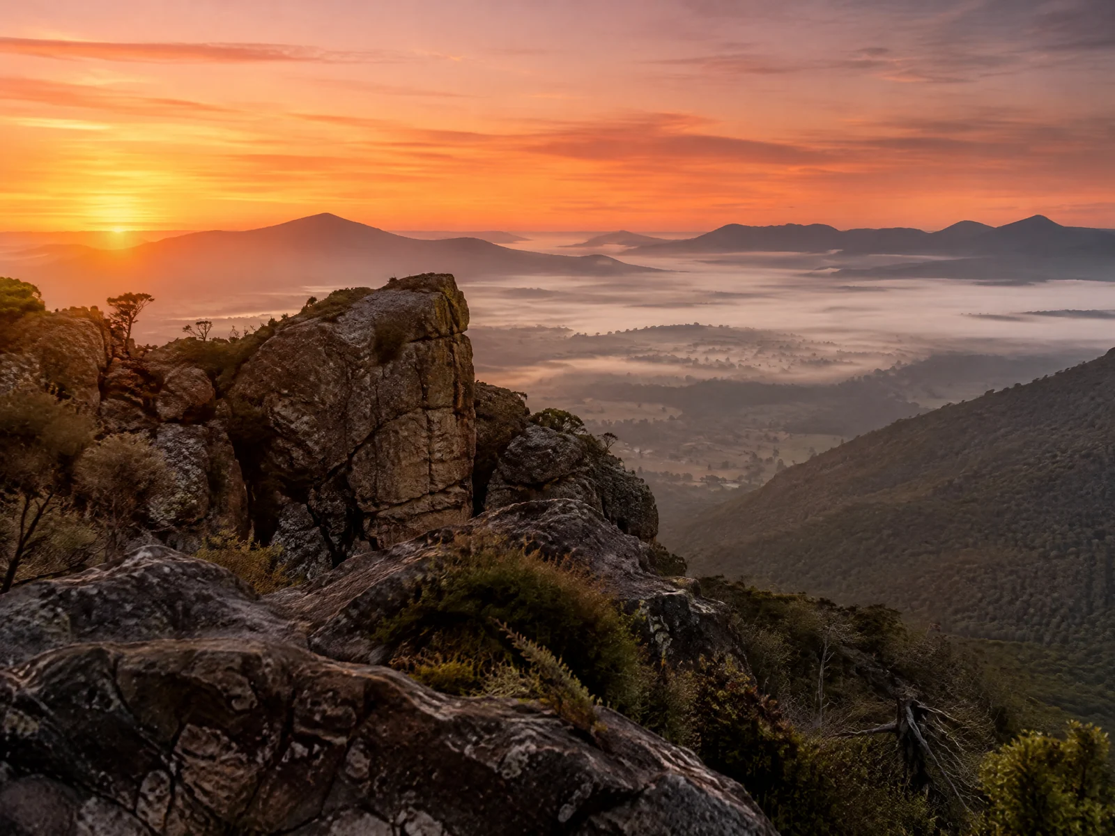 Sunrise over the Grampians sandstone ranges with orange sky and misty valley below the rock formations