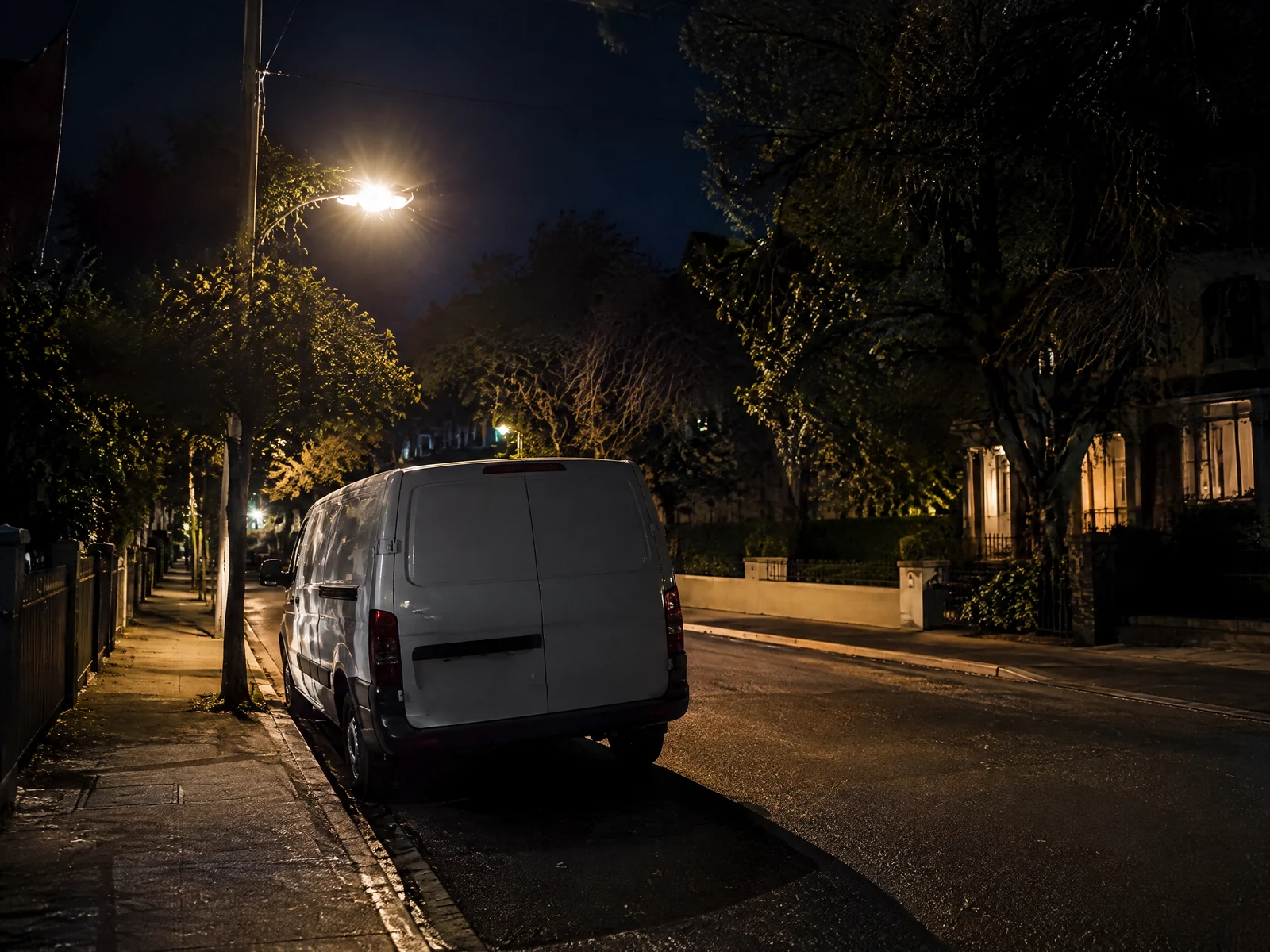 White van parked on a quiet city street at night under a streetlight
