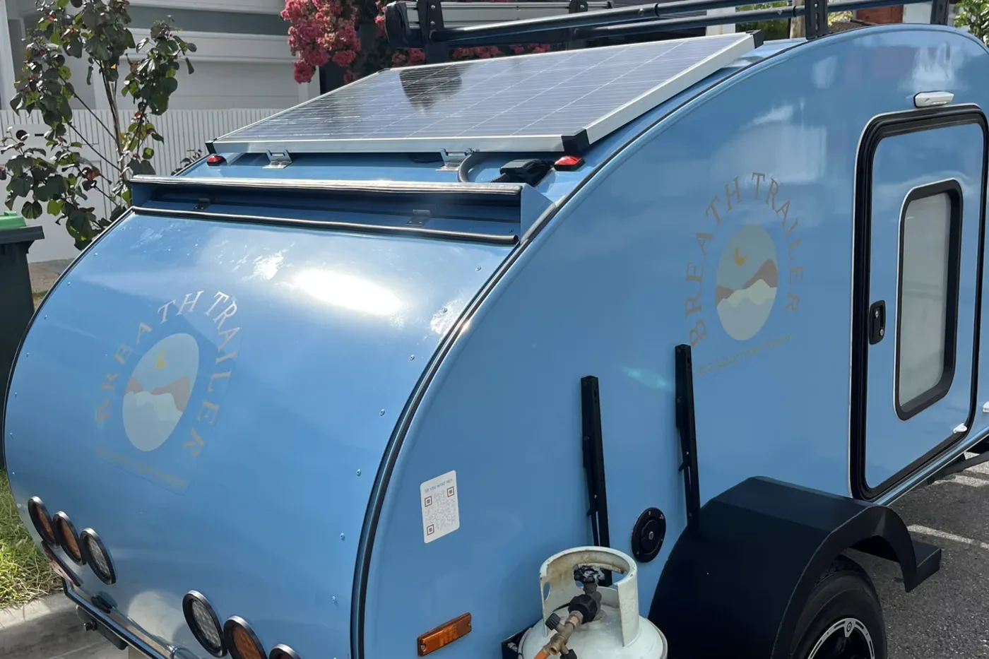 Sky blue compact Breath teardrop with roof-mounted solar panel and gas bottle parked on a suburban street