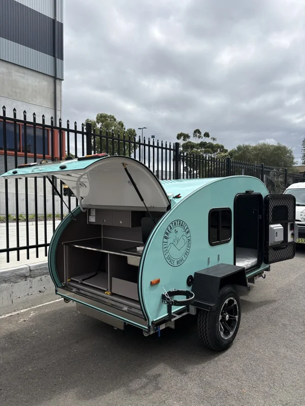 Mint compact Breath teardrop with rear galley hatch and side door open in a car park