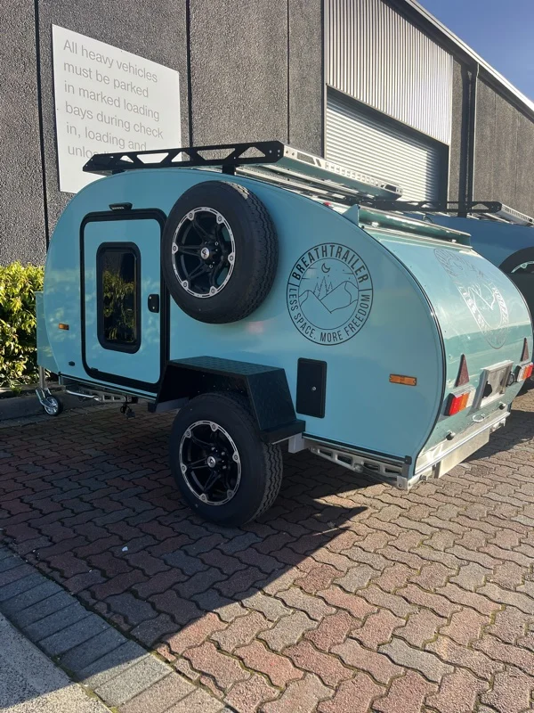 Mint compact Breath teardrop with spare wheel, roof rack and chequer-plate fender parked on brick paving