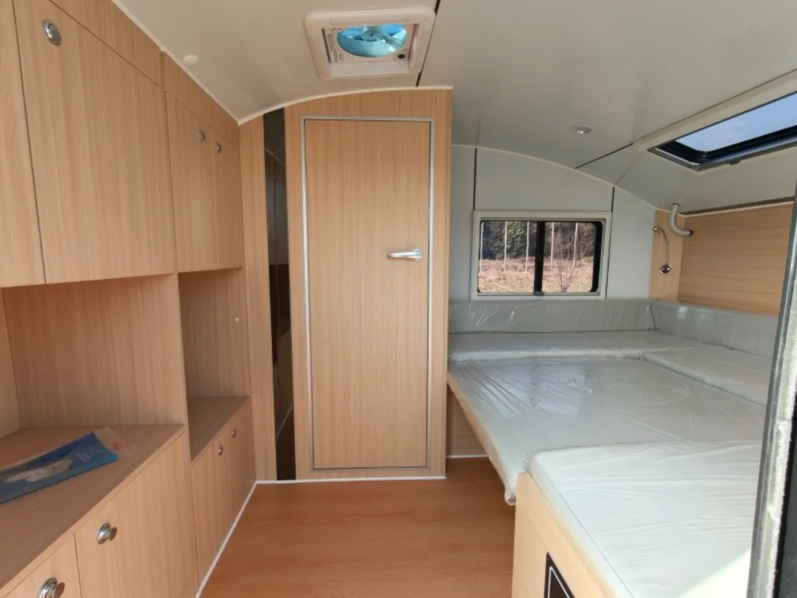 Breath Max interior with timber-look cabinets, bathroom door, roof fan and bed under a skylight