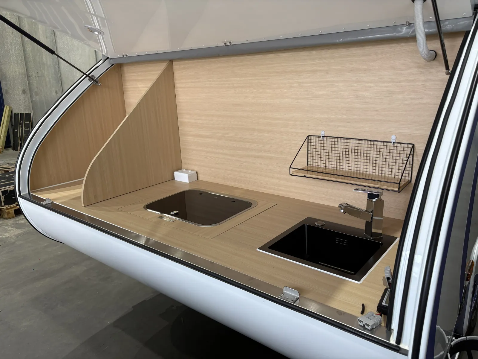 Breath Max rear galley with hatch raised, timber-look benchtop, glass-lidded cooktop, black sink and wire shelf