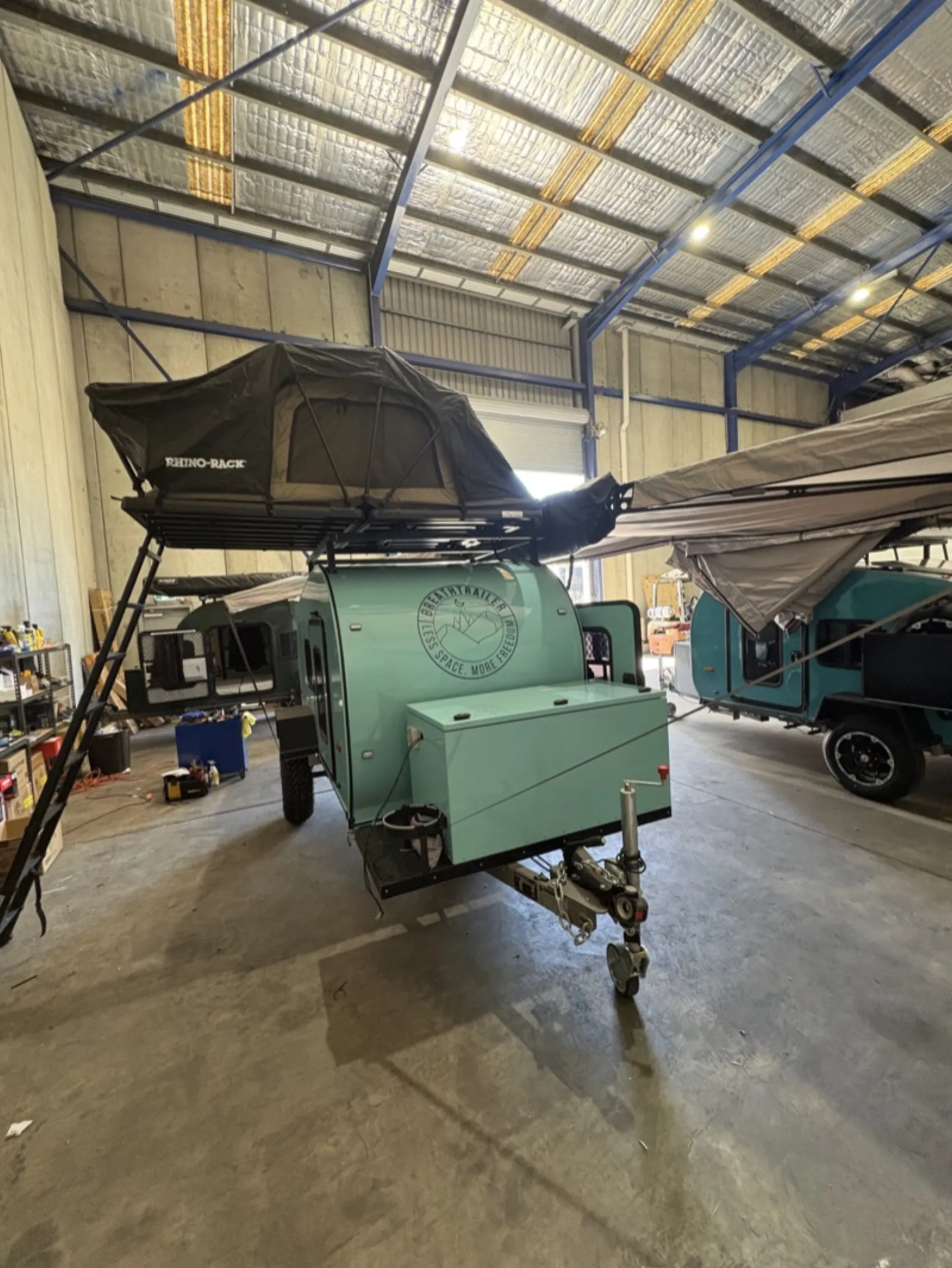 Breath Ultra in mint green with rooftop tent and ladder inside a workshop with other trailers