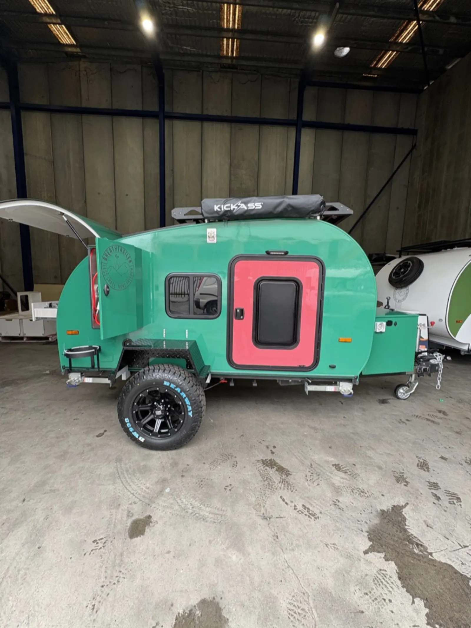 Breath Ultra in green with red door, roof rack, rolled awning and rear hatch raised, side profile in a workshop