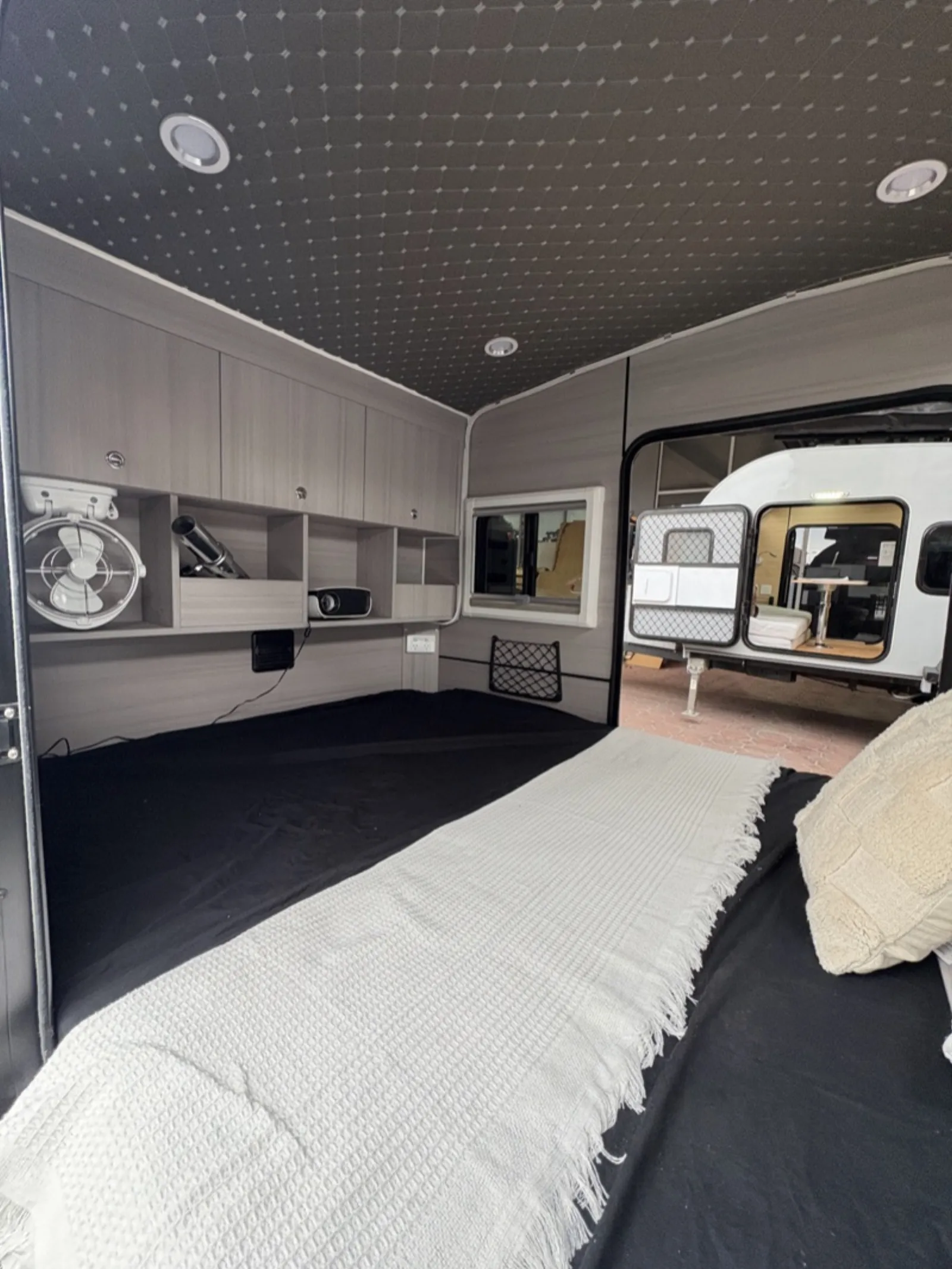 Breath Ultra interior with made-up bed, white throw, overhead cabinets, cubbies, fan and projector on the shelf