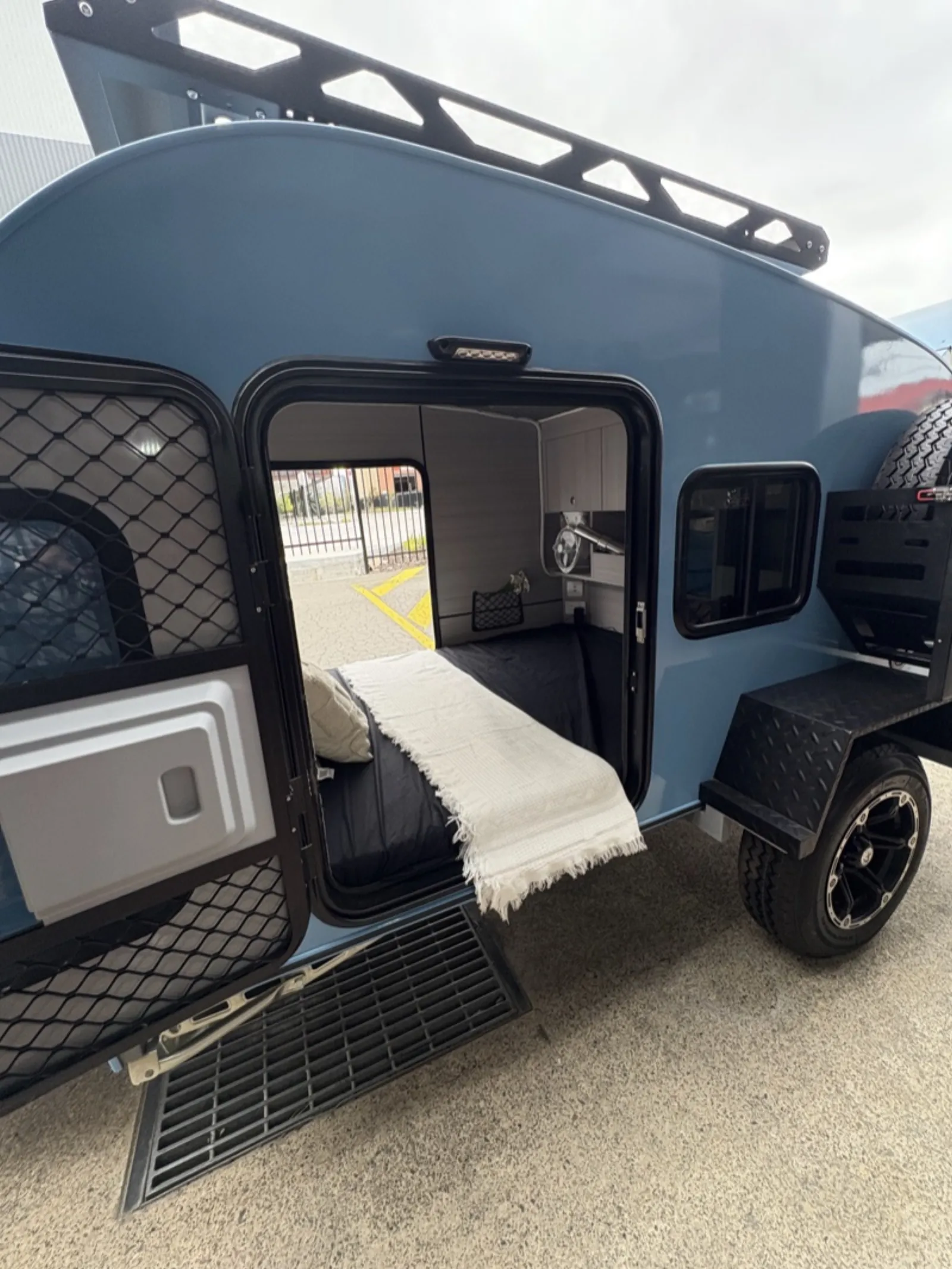 Breath Ultra in blue with side door open to a made bed with dark sheet and white throw