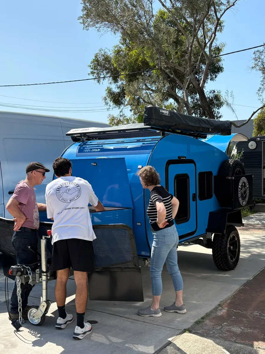 Breath Trailer team member showing a blue Breath teardrop camper to two customers outside the Sydney showroom