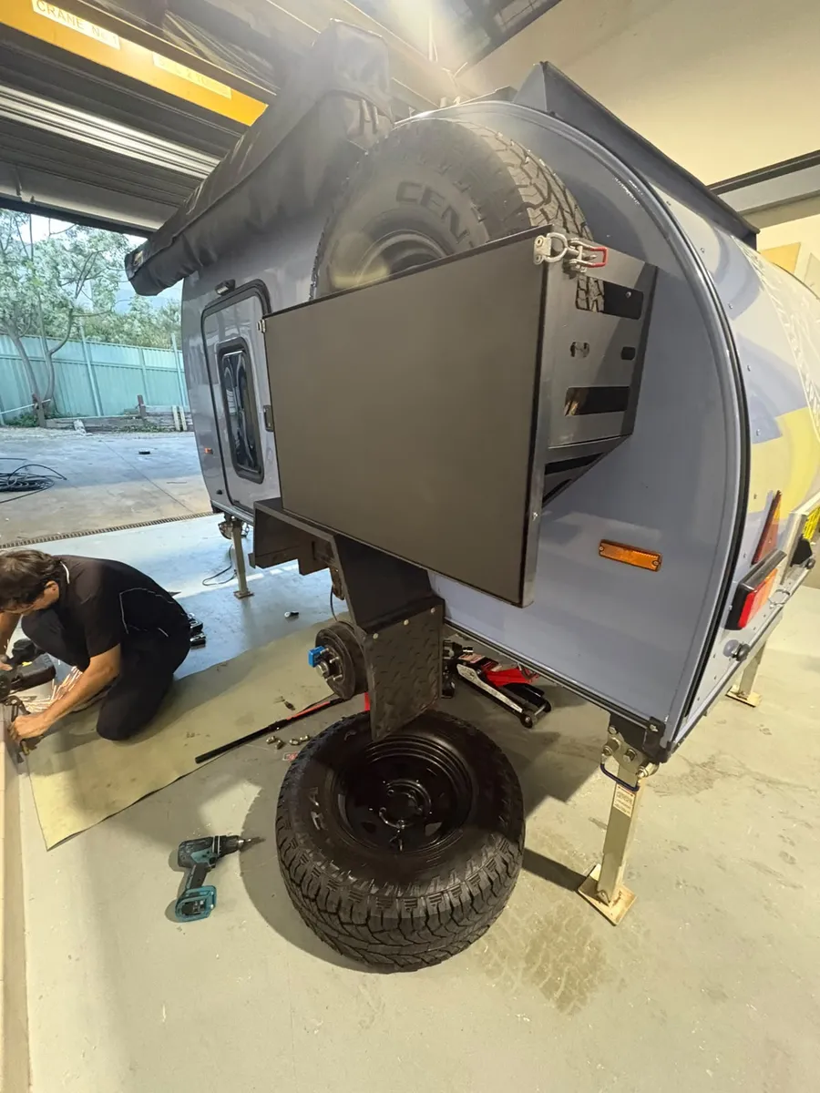Breath Trailer team member fitting a rear carrier and spare wheel to a blue Breath teardrop camper in the Sydney workshop