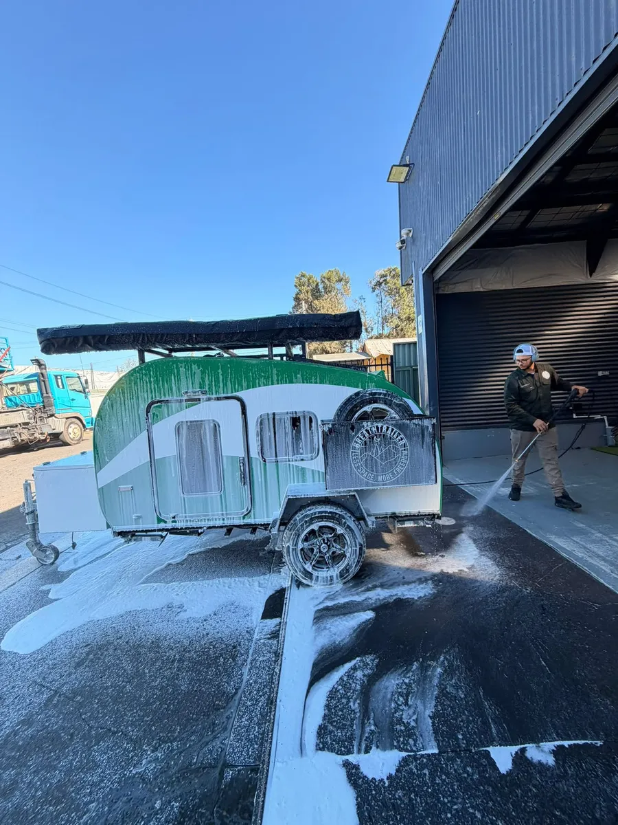 Breath Trailer team member pressure-washing a green Breath teardrop camper outside the Sydney workshop